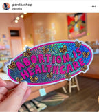 A vinyl bumper sticker with glitter detail, featuring butterflies surrounding the text 'Abortion is Healthcare’. - The Peach Fuzz