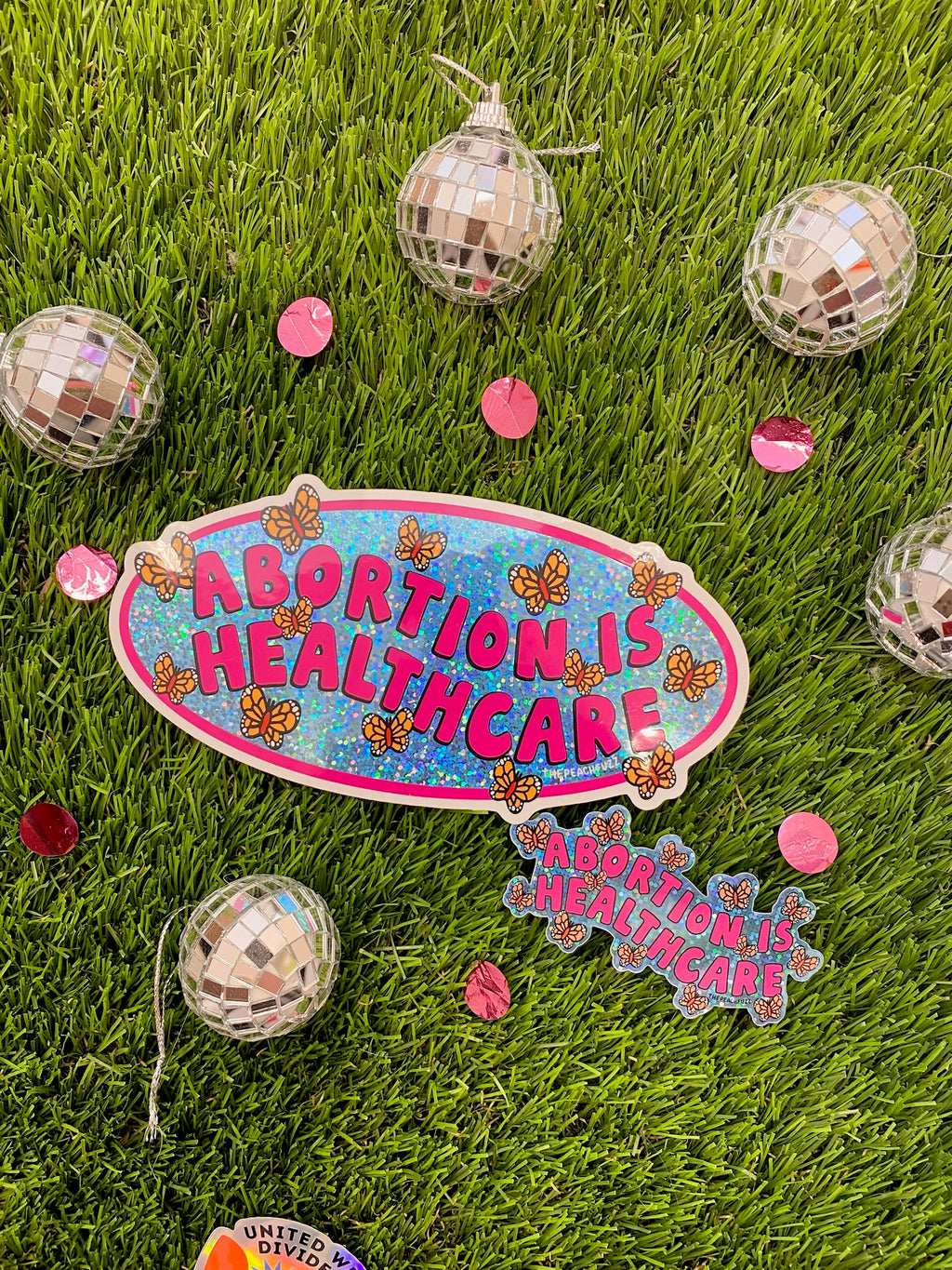 “Abortion Is Healthcare” Vinyl sticker with glossy finish and glitter detail. Measures 3.3 x 1.7 inches. - The Peach Fuzz
