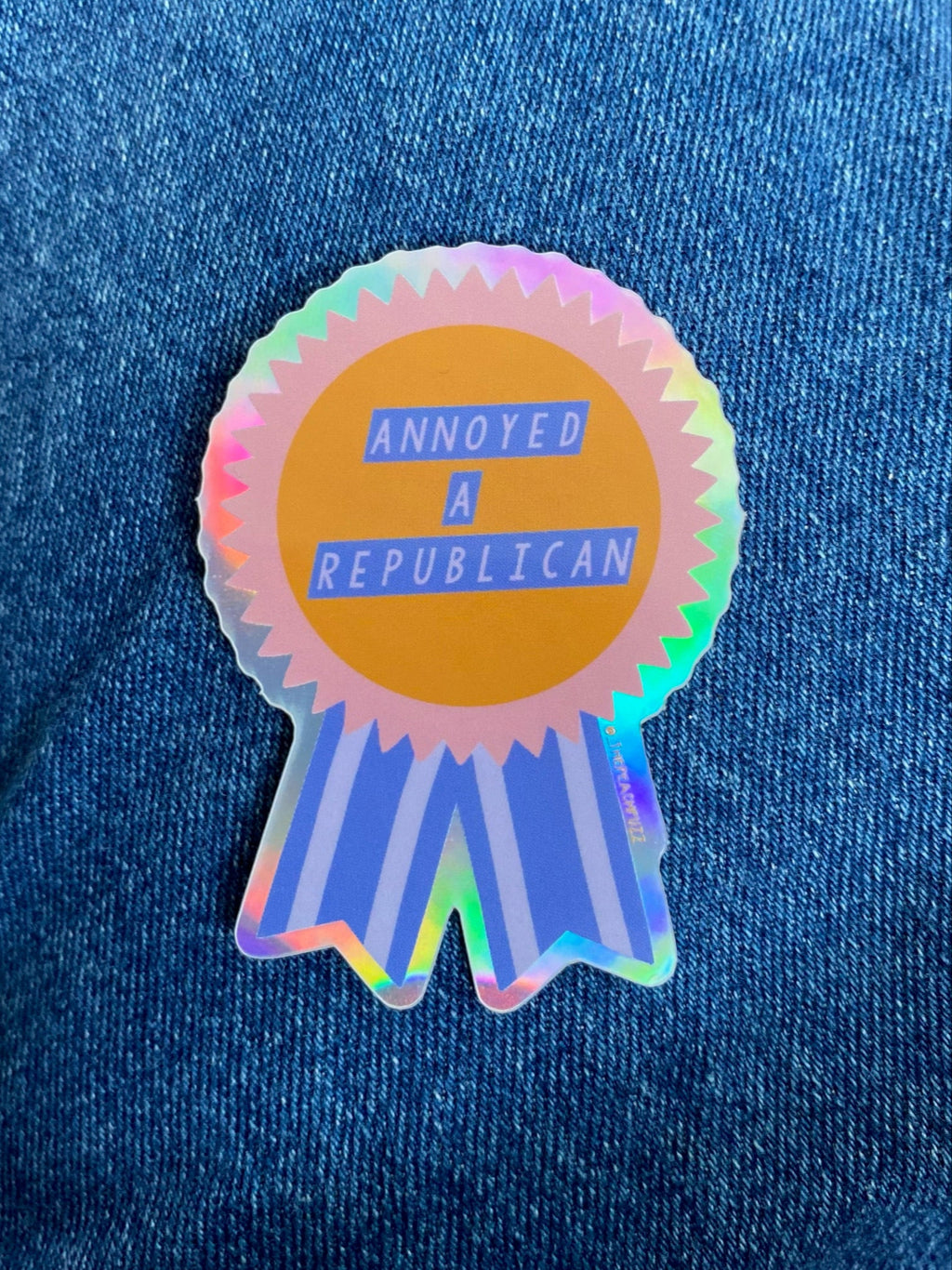 “Annoyed a Republican” Vinyl sticker with a glossy finish and a holographic outer border. Measures 1.9x2.7 inches.
