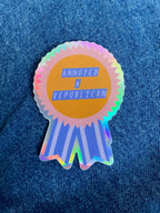 “Annoyed a Republican” Vinyl sticker with a glossy finish and a holographic outer border. Measures 1.9x2.7 inches.
