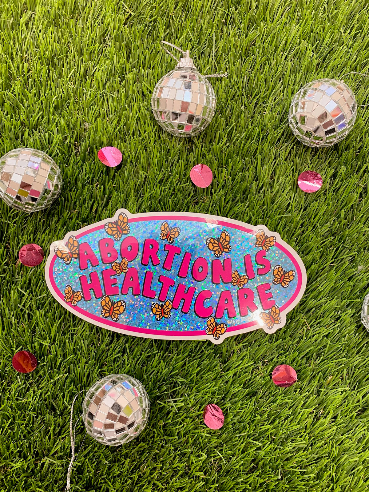 A vinyl bumper sticker with glitter detail, featuring butterflies surrounding the text 'Abortion is Healthcare’. - The Peach Fuzz