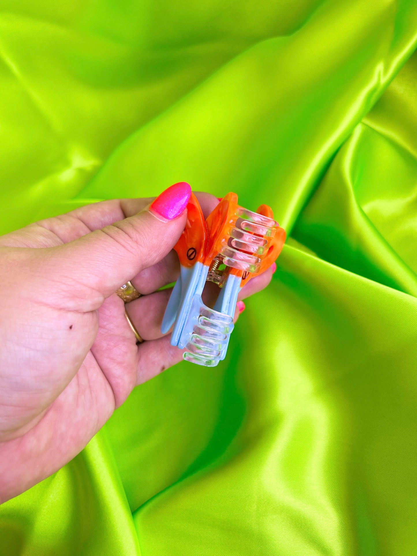 Hand holding Mini Scissors Hair Claw against a green fabric background