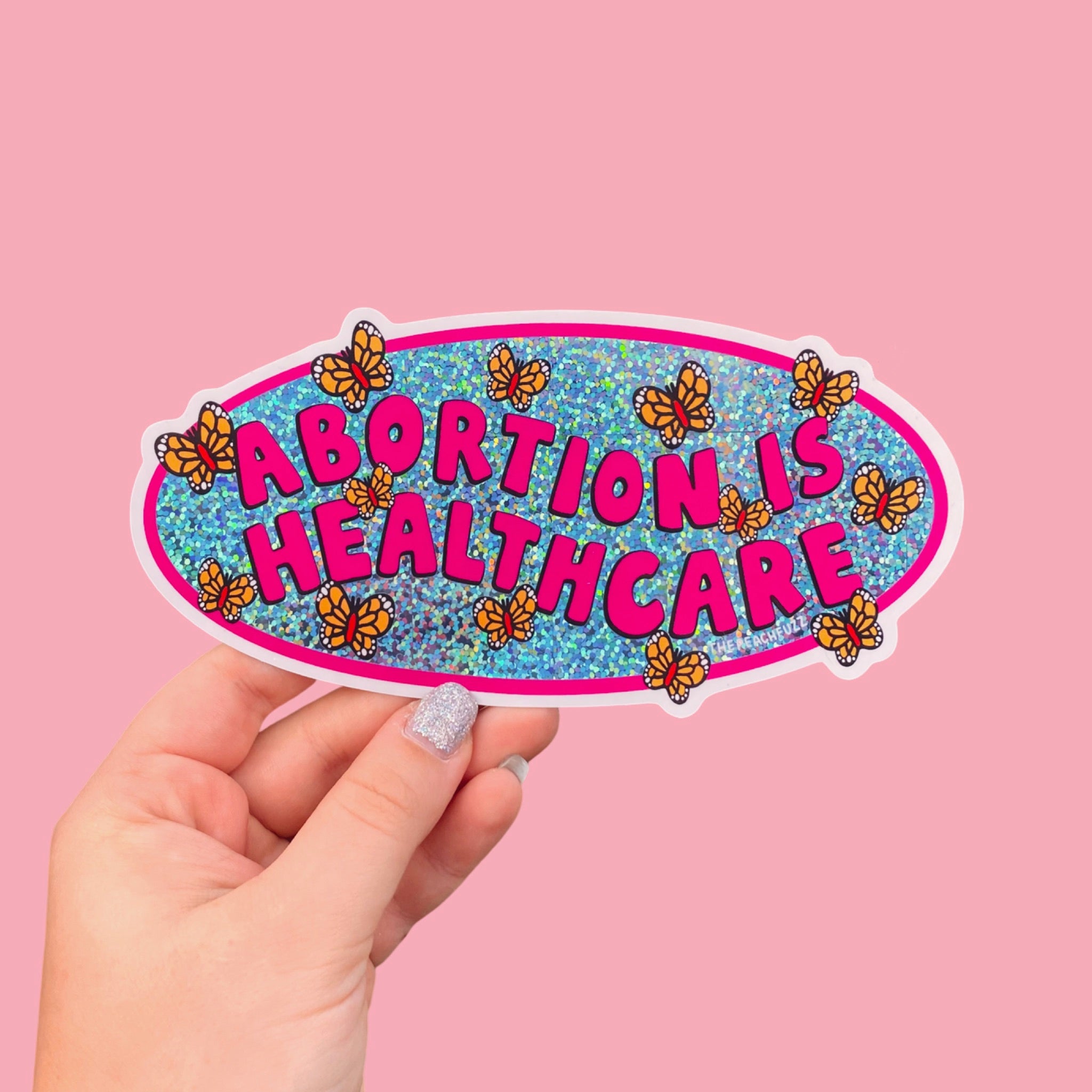 A vinyl bumper sticker with glitter detail, featuring butterflies surrounding the text 'Abortion is Healthcare’. - The Peach Fuzz