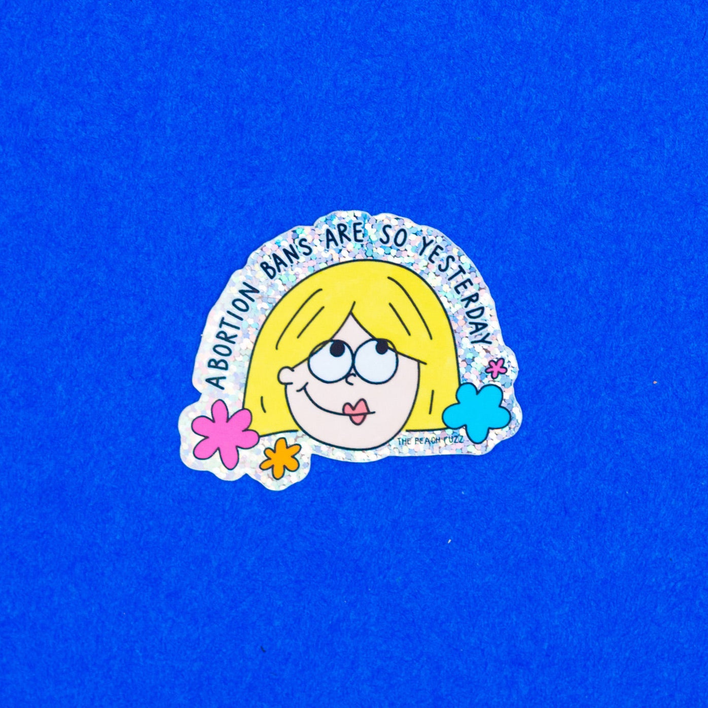 A vinyl sticker with glitter detail, featuring an illustration of a character with blonde hair, and the text 'Abortion bans are so yesterday’. - The Peach Fuzz