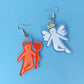 A pair of earrings made of acrylic featuring a poorly drawn angel and devil
