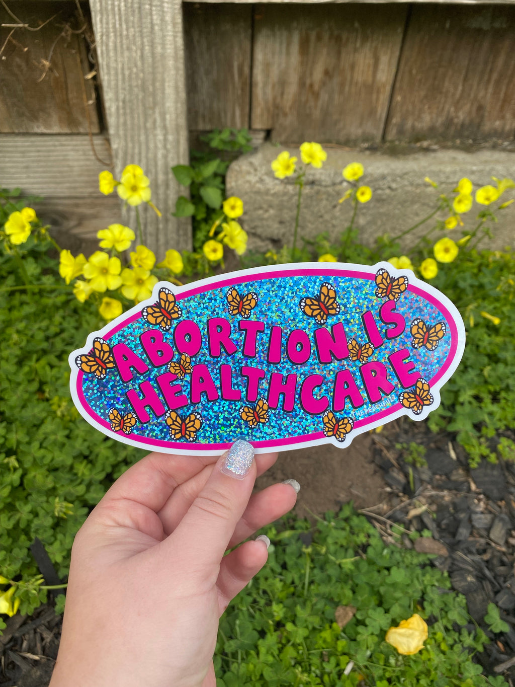 A vinyl bumper sticker with glitter detail, featuring butterflies surrounding the text 'Abortion is Healthcare’. - The Peach Fuzz